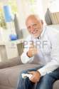 7899224-older-man-sitting-on-couch-giving-thumb-up-while-playing-computer-game-looking-at-camera-smiling.jpg